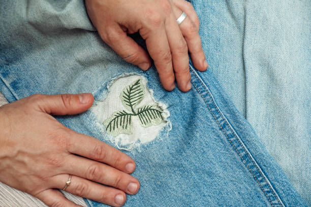 A woman mends jeans, sews a patch on a hole, hands close-up.Mending clothes concept,reusing old jeans