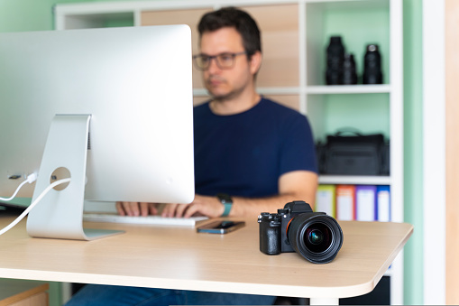 Portrait of photographer in his office working on the computer with a camera on the table