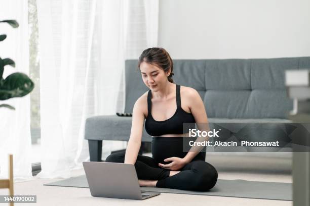 Pregnant Asian Woman Is Using Her Computer Laptop For Class Online Yoga To Keep Her Prenatal Healthy In The Living Room Stock Photo - Download Image Now