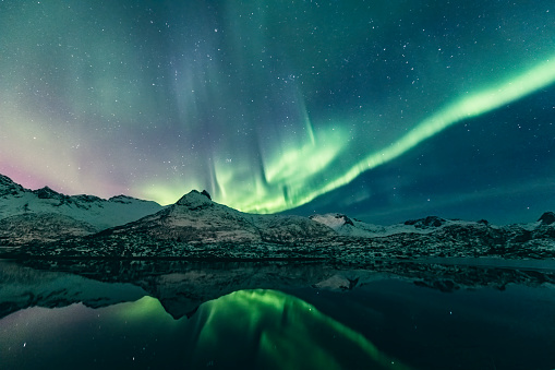 Northern Lights, polar light or Aurora Borealis in the night sky over the Lofoten islands in Northern Norway. Wide panoramic image with snow covered mountains and a lake in the foreground. The Lofoten archipelago in the county of Nordland, Norway has a spectacular scenery with dramatic mountains rising up from the open sea, Fjords and beaches.