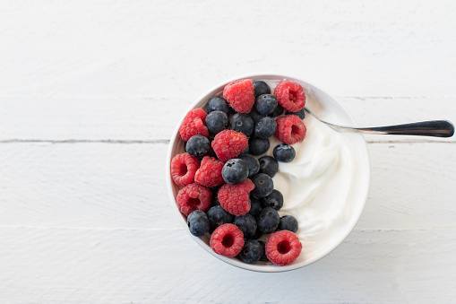 Natural and healthy protein snack with islandic skyr and fresh berries. Served in a bowl with spoon isolated on white wooden background with copy space from above