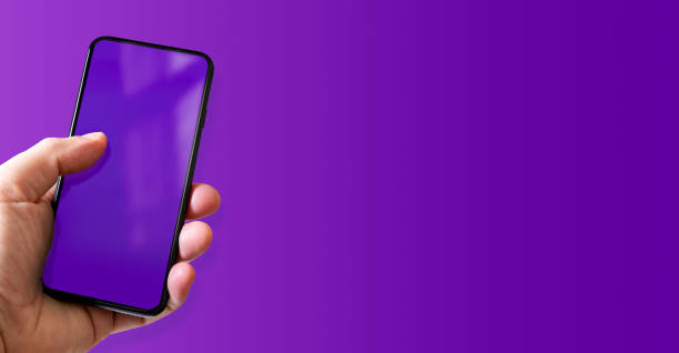 istock Hand holding a smartphone with blank purple screen. Colorful horizontal banner. 1440195897