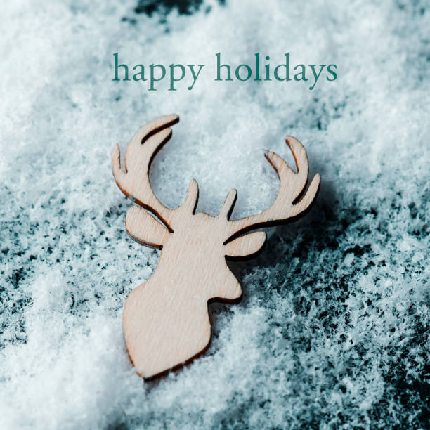 high angle view of a reindeer head cut out on wooden on the snow and the text happy holidays
