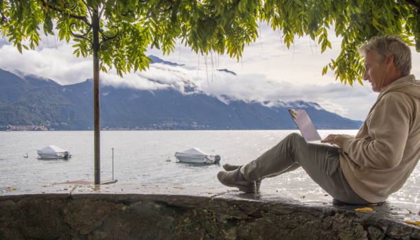 istock Man uses laptop under tree canopy on lakeshore 1440199740