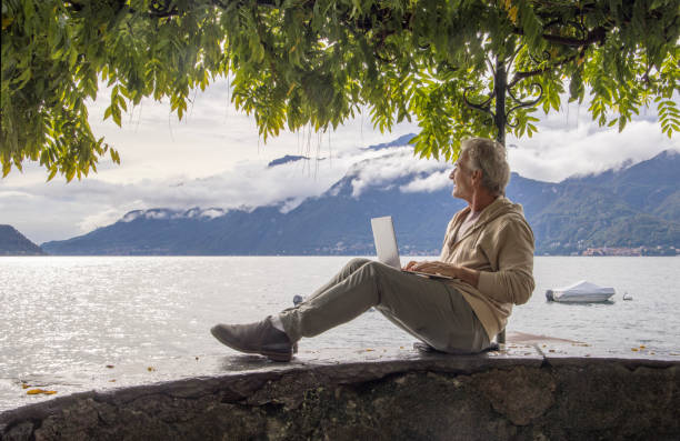 istock Man uses laptop under tree canopy on lakeshore 1440199818