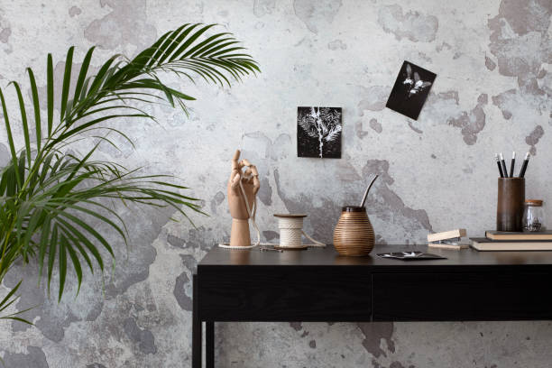 istock Creative composition of home office interior with black desk, image on wall, cup, sculptire, books, mug, pencil holder, gray concrete wall and office accessories. Home decor. Template. 1440201357