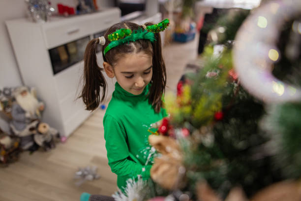 A close-up view of a lovely little girl decorating a Christmas tree at her home in the living room.