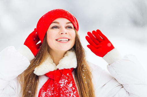 girl in winter clothes with beautiful makeup looking up and holding hands in gloves near red hat