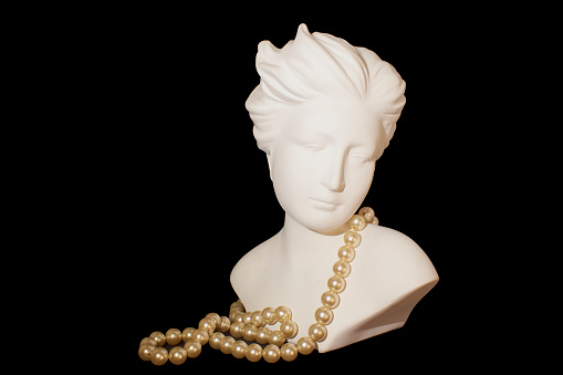 Close-up of a woman bust with pearl necklace on the neck and black background