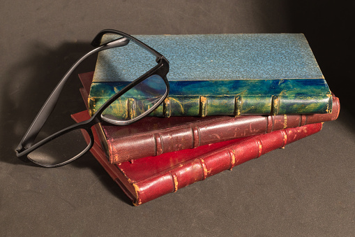 Open vintage book notepad with blank pages and glasses lie on a stack of old shabby books in a super cover on a gray concrete table