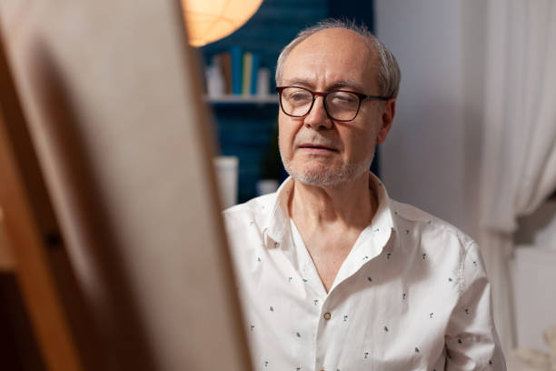 ritratto in primo piano dell'artista in pensione che guarda ispirato alla tela sul cavalletto mentre disegna usando la matita - romania men artist portrait foto e immagini stock