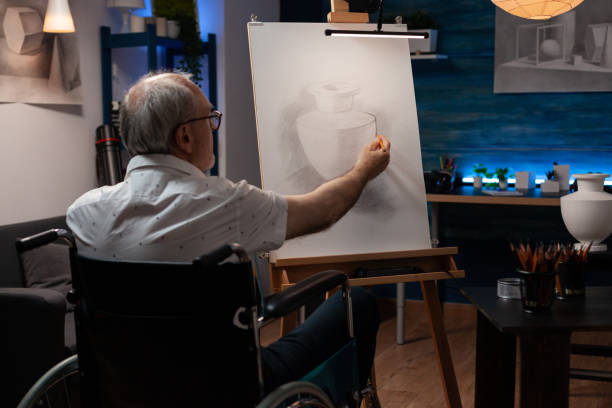 artista dell'uomo anziano che utilizza il disegno a matita originale della sedia a rotelle del vaso di natura morta sensazione creativa sul cavalletto - romania men artist portrait foto e immagini stock