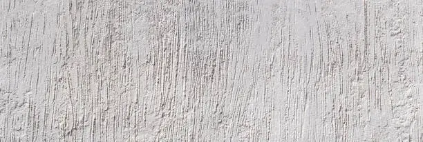 Light gray plaster with abstract pattern of rough vertical grooves in panoramic close-up