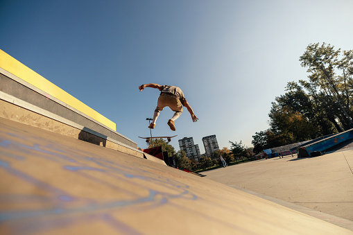 A skater is exercising at the skatepark on the bank ramp with his skateboard.