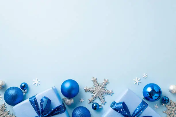 Photo of Christmas Eve concept. Top view photo of blue and silver baubles snowflake ornaments stylish present boxes and confetti on isolated pastel blue background with copyspace