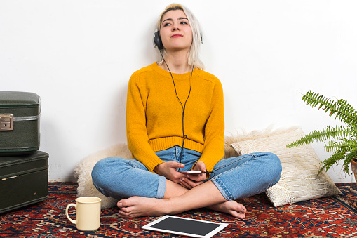 Young woman with headphones listening to music while sitting on floor in living room