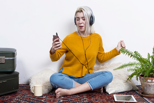 Young woman with headphones listening to music while sitting on floor in living room