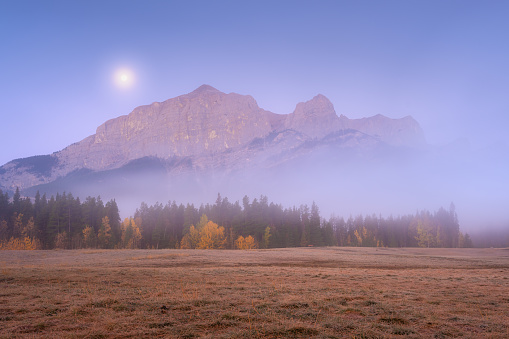Mountain landscape at dawn. Fog in a valley. Field and forest in a mountain valley at dawn. Natural landscape with bright moon light. High rocky mountains. Banff National Park, Alberta, Canada.