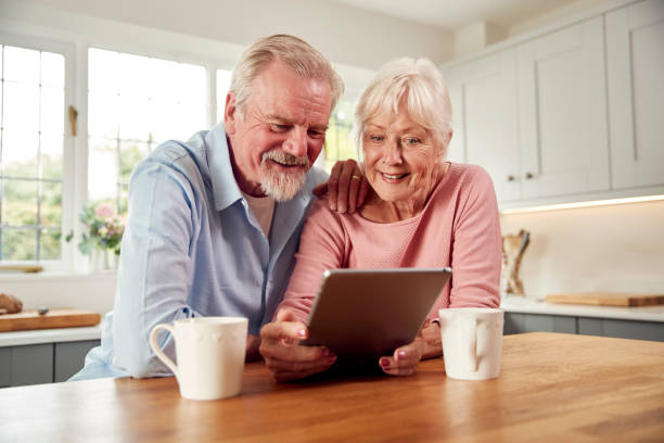 Retired Senior Couple Sitting In Kitchen At Home Drinking Coffee And Using Digital Tablet stock photo