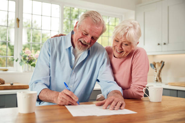 Retired Senior Couple Sitting In Kitchen At Home Signing Financial Document stock photo