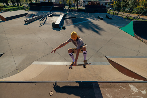 A Caucasian skater is jumping with his skateboard on the quarter pipe ramp in the skatepark on a sunny day. He is flying through the air.