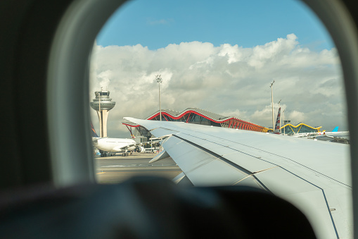 View through the window of an airplane on the runway preparing to turn back as it passes near the control tower and passenger terminal.