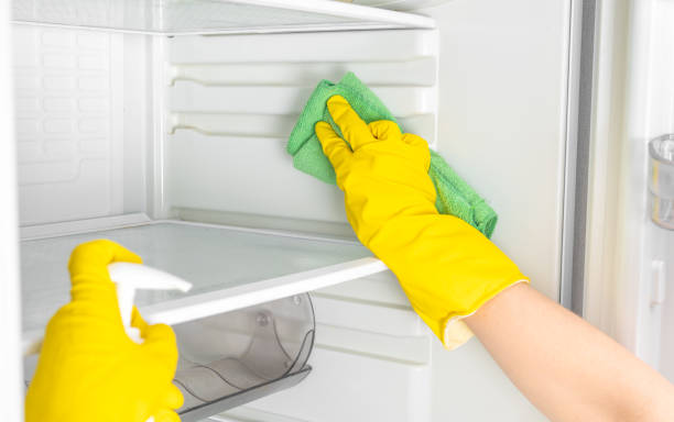 Deep Cleaning service. Woman hand in yellow rubber protective glove cleaning white open empty refrigerator with green rag. Spray for windows and glass surfaces cleaner Woman hands in yellow rubber protective glove and green sponge washes, cleans refrigerator shelves. Deep Cleaning service. House cleaning, spray bottle with detergents for washing fridge. deep cleaning services stock pictures, royalty-free photos & images