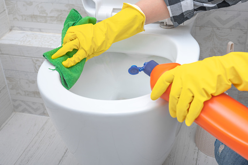 Close up hand with detergent cleaning toilet bowl in bathroom. Man in yellow rubber gloves cleaning toilet seat with green cloth. Bathroom and toilet hygiene. Hand cleaning toilet bowl in bathroom