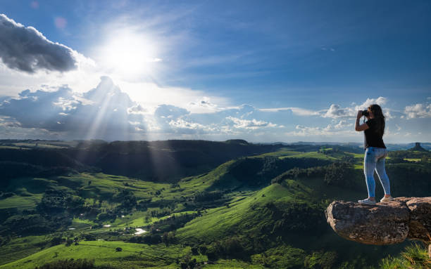 Photographing the landscape at sunset, Ribeirão Claro, Parana State, Brazil Young woman photographing the landscape at sunset from the Morro do Gavião, Ribeirão Claro, Brazil hanging stone stock pictures, royalty-free photos & images
