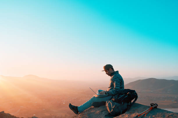 mature latin man on top of the hill with a laptop working outdoors at sunset stock photo