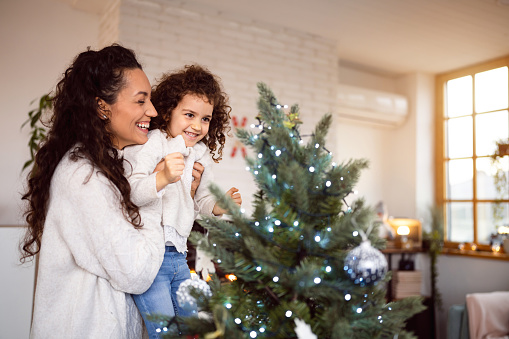 Caucasian mother and daughter decorating Christmas tree together