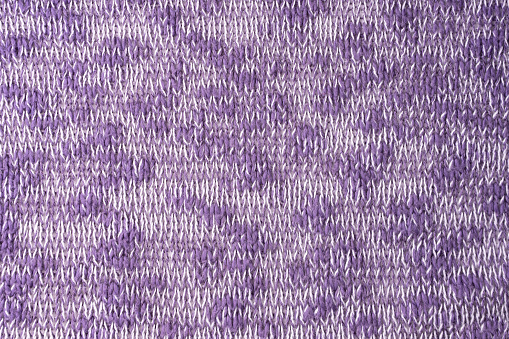Close up background of knitted wool fabric made of viscose yarn. Mix of purple and white color, melange wool knitwear texture. Abstract knitted jersey background. Fabric abstract backdrop, wallpaper