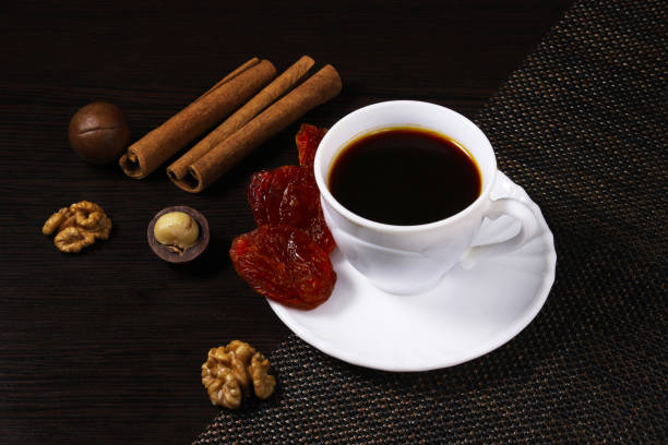 A cup of black coffee on a dark table with nuts, cinnamon and dried fruit. Shallow depth of field