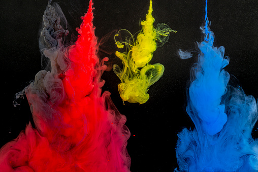 A needles from which the red, yellow, blue and gray paint flows into bowl of water on a black background