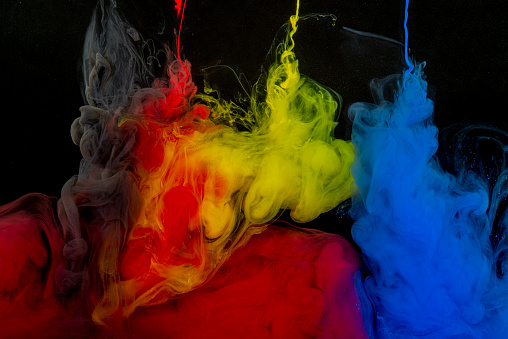 A needles from which the red, yellow, blue and gray paint flows into bowl of water on a black background