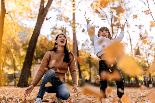 Mother and daughter playing in park, throwing tree leaves