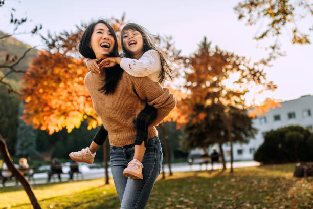 Shot of an adorable little girl enjoying a piggyback ride with her mother in public park stock photo