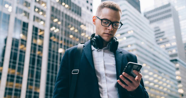 istock Formal executive surfing smartphone while using headphone on street 1440253329