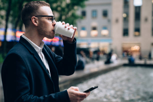 istock Businessman drinking coffee and looking away while using smartphone 1440253363