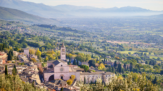 A beautiful landscape of the green Umbria Valley with in the foreground the Basilica di Santa Chiara (Basilica of Saint Clare) and a glimpse of the medieval city of Assisi. Built in the Italian Gothic style in 1257, the Basilica of Santa Chiara preserves the mortal remains of the saint and the famous Crucifix of San Damiano, in front of which St. Francis discovered his vocation. Over the centuries Assisi and the spirituality of these places have become a world reference point for peace, tolerance and solidarity between peoples and different confessions. The Umbria region, considered the green lung of Italy for its wooded mountains, is characterized by a perfect integration between nature and the presence of man, in a context of environmental sustainability and healthy life. In addition to its immense artistic and historical heritage, Umbria is famous for its food and wine production and for the high quality of the olive oil produced in these lands. Since 2000 the Basilica and other Franciscan sites of Assisi have been declared a World Heritage Site by UNESCO. Image in 16:9 and high definition format.
