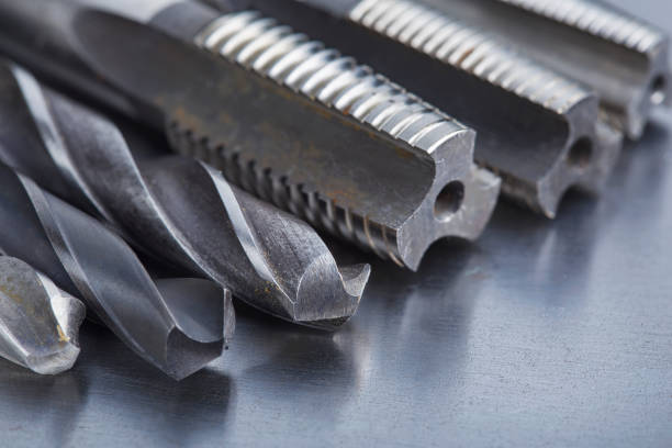 set of different drill bits,thread tap and mill cutters with caliper ruler on steel plate background. Locksmithing deal.