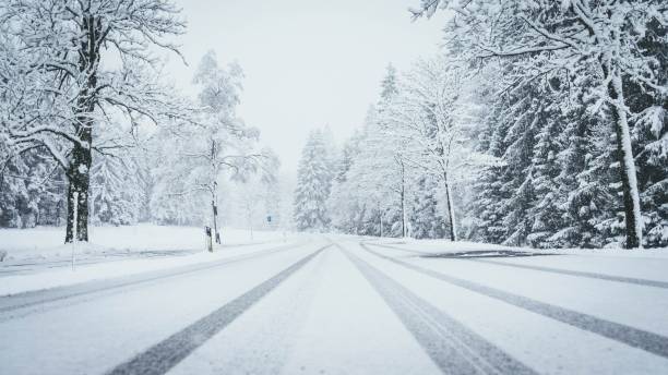 plan large d'une route entièrement couverte par la neige avec des pins sur les deux côtés et des traces de voiture - winterroad photos et images de collection