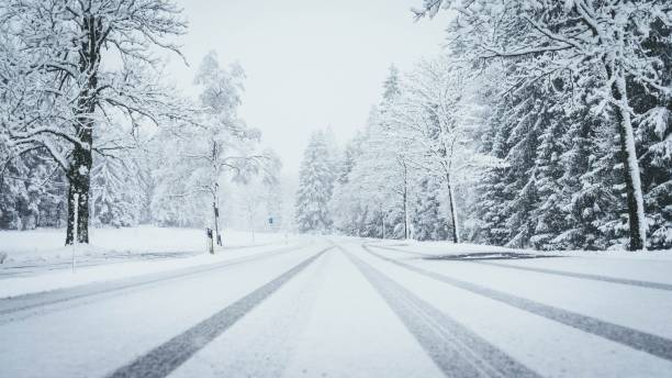 tiro largo de uma estrada coberta inteiramente pela neve com as árvores de pinho em ambos os lados e em traços do carro - snowing road winter snow - fotografias e filmes do acervo