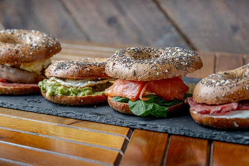 A close-up of Bagels with cream cheese, smoked salmon, eggs, bacon and avocados on rustic wooden background