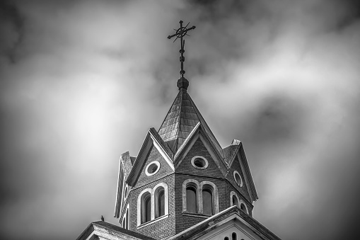 A low angle greyscale shot of the top of a Christian church with cloudy sky in the background