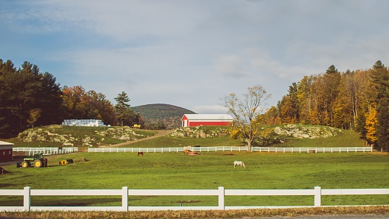 A wide shot of a beautiful large ranch with tractors and horses grazing the grass with a red barn in the distance