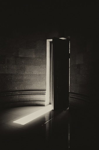 A half-open wooden door of a Christian church shot in black and white