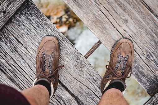 An overhead shot of a male feet standing on a wooden bridge wearing hiking shoes