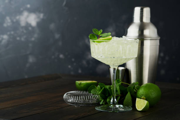 istock Margarita cocktail with lime, tequila, mint and ice on dark table with amazing backlight, copy space. Classic Margarita or Daiquiry Cocktail. Bar card or counter concept. Selective or soft focus. 1440267087