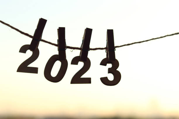 Wooden number hang on rope attached with clothes peg pins over orange morning sky sunrise and blurred city bokeh light background. Happy New Year 2023 celebration for brighter start day concept. número de madera colgado de una cuerda unida con alfileres de pinza de ropa sobre el amanecer naranja del cielo de la mañana y el fondo borroso de la luz bokeh de la ciudad. feliz celebración de año nuevo 2023 para un concepto más brillante del día d